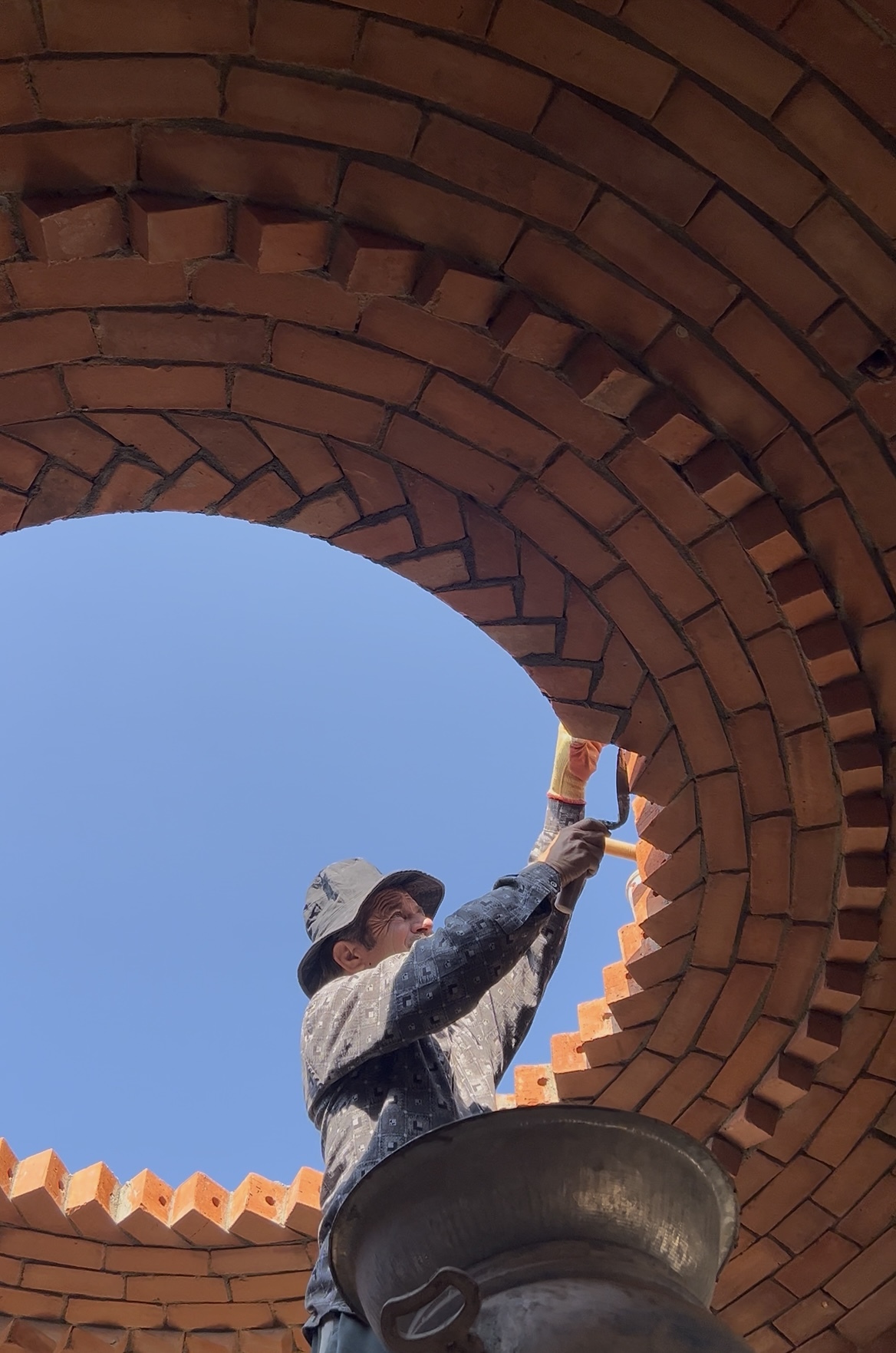 Worker finishing circular opening in dome from below - Rohtak Domes 2025